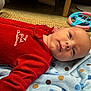 baby, infant, red_clothing, blanket, polka_dot, toy, steering_wheel, floor, carpet, laying_down, face, cute, holiday, christmas, child, indoors, portrait, expression, person, young