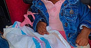 Ayanna is registered to the contest to win money with this photo: baby, infant, child, car_seat, sitting, denim_jacket, pink_clothing, blanket, pink_cup, wide_eyed, portrait, indoor, vehicle, safety_harness, dark_hair, brown_skin, looking_away, colorful, cozy, photograph