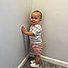 toddler, child, boy, standing, corner, wall, carpet, smile, clothing, shirt, shorts, shoes, indoor, curly_hair, cute, happy, person, portrait, casual, light