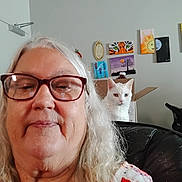 Ivory is registered to the contest to win money with this photo: woman, selfie, glasses, white_hair, cat, heterochromia, couch, painting, wall_art, box, indoor, portrait, senior, smile, home, furniture, light, curious, pet, relax