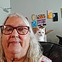woman, selfie, glasses, white_hair, cat, heterochromia, couch, painting, wall_art, box, indoor, portrait, senior, smile, home, furniture, light, curious, pet, relax
