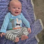 Leo is registered to the contest to win money with this photo: baby, child, smiling, blue_shirt, striped_pants, blanket, purple, soft_texture, happy, cute, infant, lying_down, clothing, face, feet, hand, indoors, person, portrait, cozy