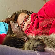 Ronan Axel is registered to the contest to win money with this photo: person, cat, kitten, sleeping, glasses, hoodie, red_clothing, face, nose_ring, indoor, bed, blanket, cozy, fur, closeup, relaxed, comfort, resting, portrait, home