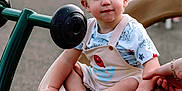Zayden is registered to the contest to win money with this photo: balance, barefoot, casual_clothing, child, curious, cute, daylight, fun, holding_hand, outdoor, overalls, park, person, play, playground, seat, short_hair, spinner, toddler, toy