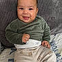 baby, smiling, child, infant, clothing, green_shirt, patterned_pants, hedgehog_pattern, couch, pillow, gray_pillow, happy, indoor, portrait, sitting, cute, face, young_child, cozy, home