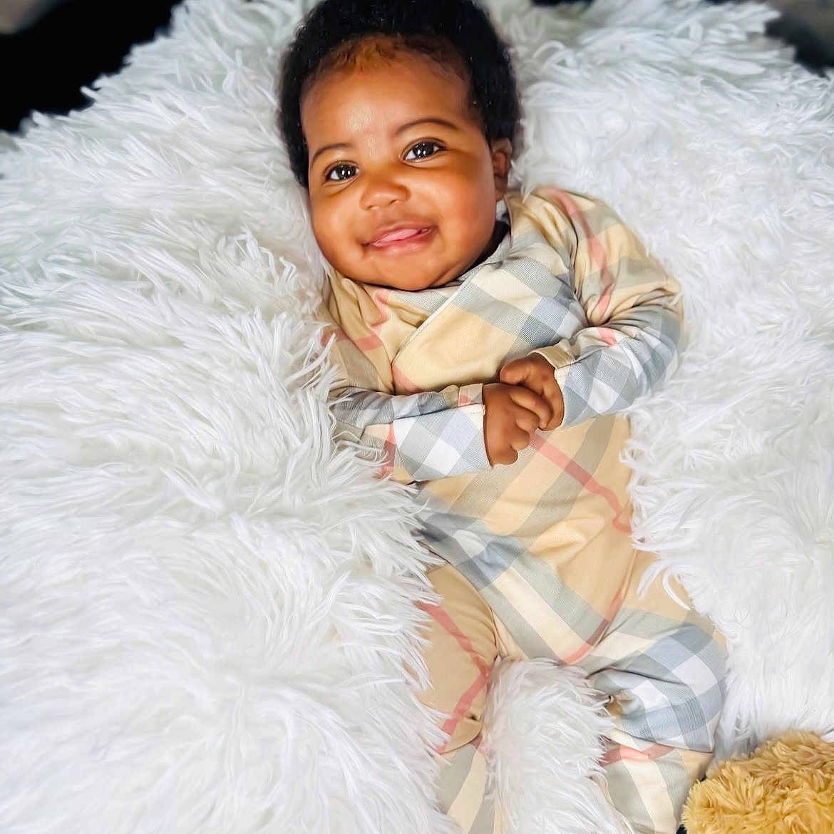 Adonis is registered to the contest to win money with this photo: baby, smiling, plaid_onesie, fluffy_blanket, infant, cute, happy, portrait, child, soft_texture, cozy, relaxed, indoor, person, skin, foot, face, hands, comfort, young