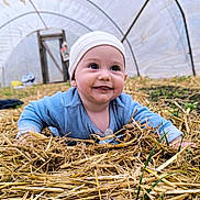 Eden a rejoint le concours — aidez-le/la à gagner de superbes lots ! baby, infant, child, smiling, straw, hay, greenhouse, tunnel, beanie, pacifier, crawling, ground, portrait, cute, outdoor, farm, grass, eyes, hands, happy