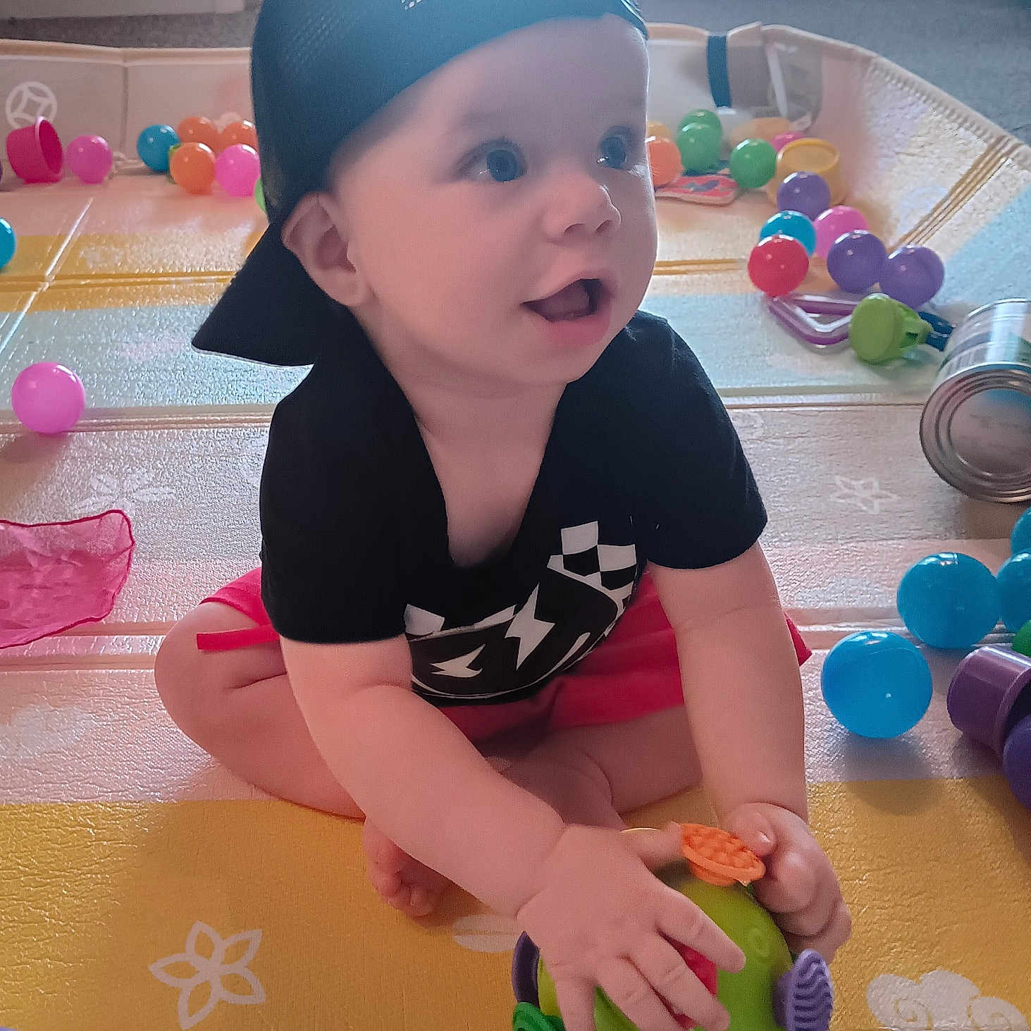 Slade joined the competition — help win amazing prizes! baby, cap, child, clothing, colorful, cute, eyes, face, floor, hand, happy, indoor, light, mouth_open, plastic_balls, play_mat, room, sitting, toy, window