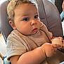 baby, child, high_chair, bib, indoor, holding, small_object, curly_hair, cute, chubby_cheeks, person, seated, casual_clothing, focused, wooden_floor, furniture, daylight, young_child, closeup, expression