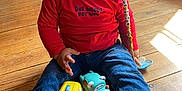 Gabin a rejoint le concours — aidez-le/la à gagner de superbes lots ! toddler, child, toy, wooden_floor, red_shirt, blue_jeans, socks, smiling, indoor, sunlight, animal_toys, pacifier, dog, home, floor, playtime, cute, happy, person, casual_clothing