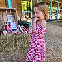 Lou a rejoint le concours — aidez-le/la à gagner de superbes lots ! child, girl, dress, red_and_white, checkered, sandals, hay, books, firewood, wooden_wall, outdoor, building, glass_door, pensive, standing, floor, necklace, summer, daylight, portrait