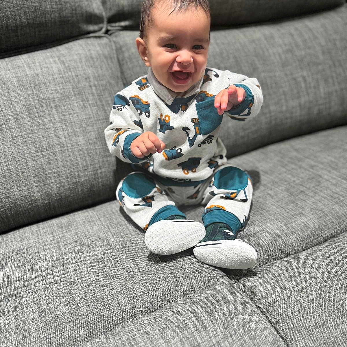 Sabar is registered to the contest to win money with this photo: baby, child, clothing, couch, cozy, cute, face, gray_couch, happy, home, indoor, infant, pants, person, portrait, shoes, sitting, smiling, sweater, young_child