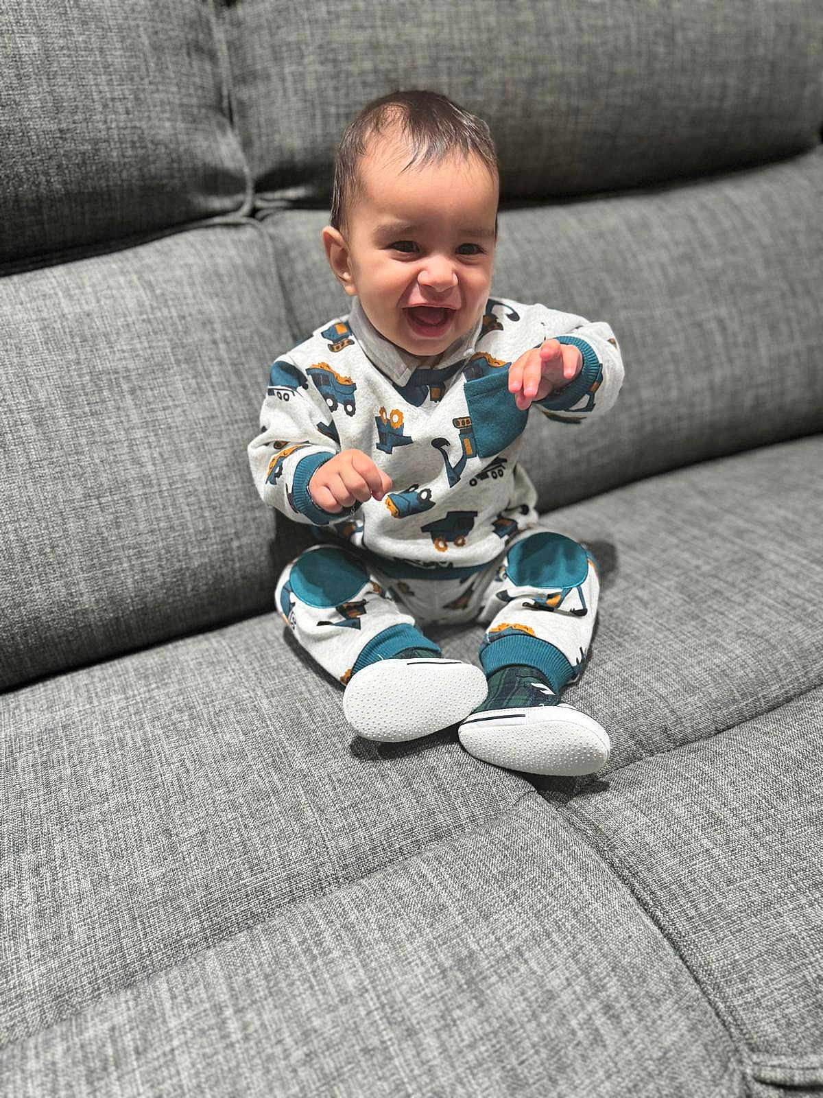 Sabar is registered to the contest to win money with this photo: baby, child, clothing, couch, cozy, cute, face, gray_couch, happy, home, indoor, infant, pants, person, portrait, shoes, sitting, smiling, sweater, young_child