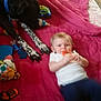 baby, blanket, blue_collar, casual, child, colorful_toys, curious, dog, floor, indoor, infant, lying_down, navy_pants, pet, pink_blanket, playtime, sniffing, toy, white_shirt, wooden_floor