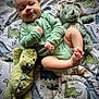 baby, infant, onesie, green_clothing, plush_toy, dinosaur_plush, blanket, dinosaur_pattern, cute, drool, smiling, lying_down, child, soft_toy, toddler, indoor, playtime, happy, face, skin