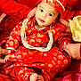 baby, child, traditional_clothing, red_outfit, hat, pearl_necklace, balloon, hands, fabric, sitting, portrait, cute, celebration, festive, infant, smiling, indoors, person, cultural, bright_colors