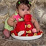 baby, child, watermelon, fruit, strawberries, banana, green_dress, hair_clips, couch, patterned_furniture, curious, cute, food, snack, indoor, portrait, sitting, colorful, playful, summer