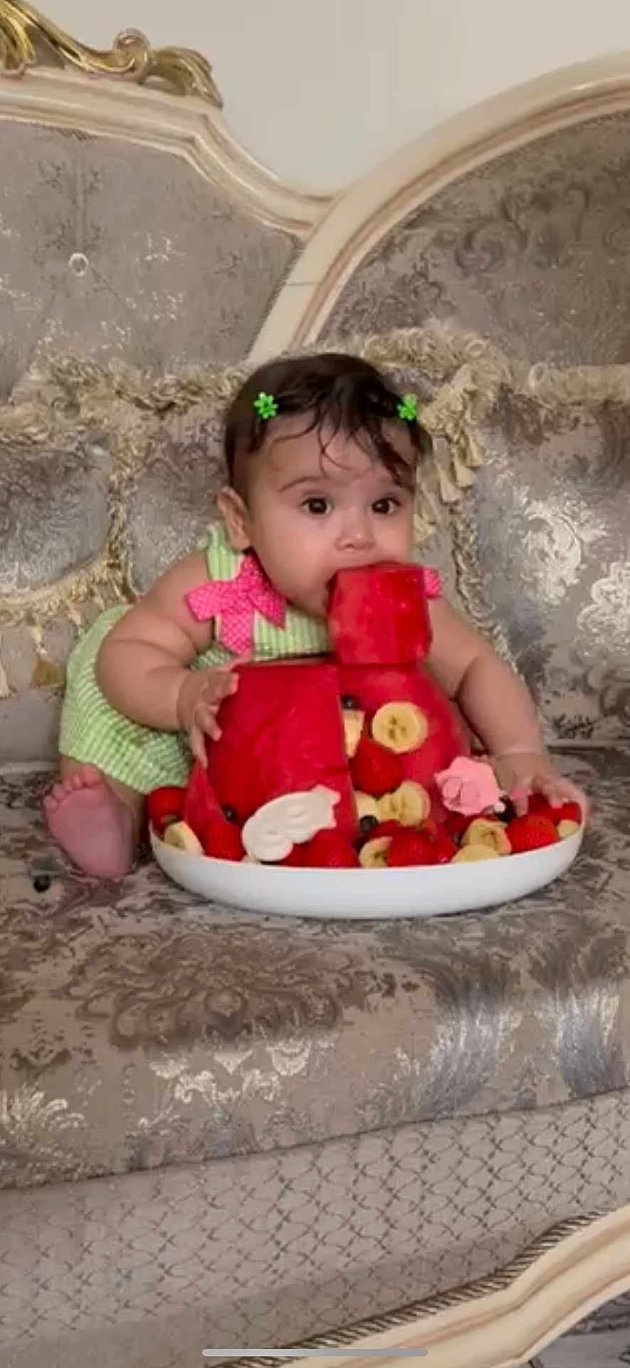 Nazli joined the competition — help win amazing prizes! baby, child, watermelon, fruit, strawberries, banana, green_dress, hair_clips, couch, patterned_furniture, curious, cute, food, snack, indoor, portrait, sitting, colorful, playful, summer