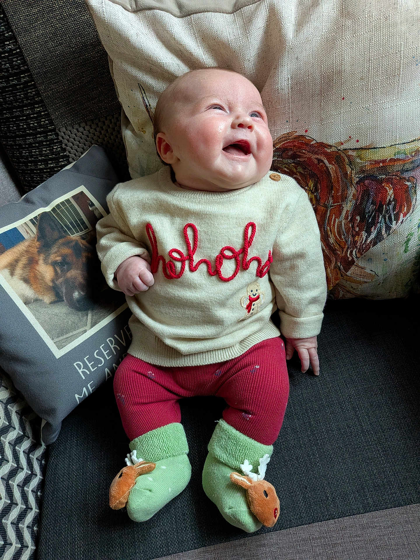 Myah is registered to the contest to win money with this photo: baby, infant, sitting, smiling, sweater, hohoho, green_socks, reindeer, couch, pillows, dog_photo, rooster_pillow, cozy, indoor, cute, holiday_theme, child, happy, portrait, clothing