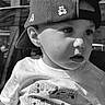 child, toddler, boy, cap, hat, teddy_bear_pattern, shirt, outdoor, portrait, black_and_white, face, expression, curious, sunlight, candid, casual_clothing, young_child, close_up, daylight, person
