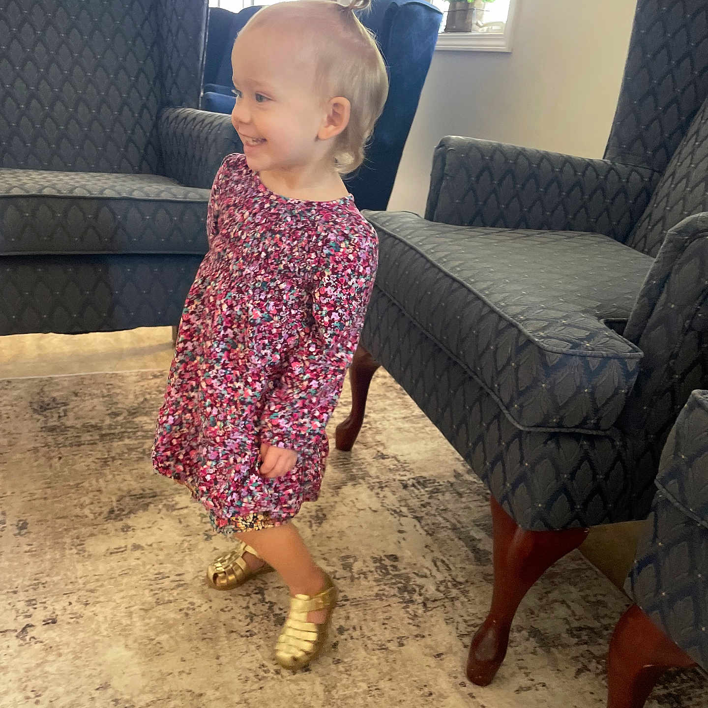 Kennedy is registered to the contest to win money with this photo: armchair, carpet, child, cute, dress, floor, furniture, golden_shoes, hair, happy, home, indoor, living_room, natural_light, person, side_view, smiling, toddler, window, young