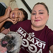 Teddy is registered to the contest to win money with this photo: woman, boy, child, dog, pet, family, selfie, portrait, smiling, happy, tongue_out, indoors, bedroom, bed, clothing, t_shirt, maroon, braces, long_hair, companionship