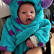 Rowan is registered to the contest to win money with this photo: baby, infant, costume, hood, monster, purple, blue, hand, indoor, cute, tongue_out, expression, clothing, person, child, soft_texture, warm, holding, funny_face, portrait