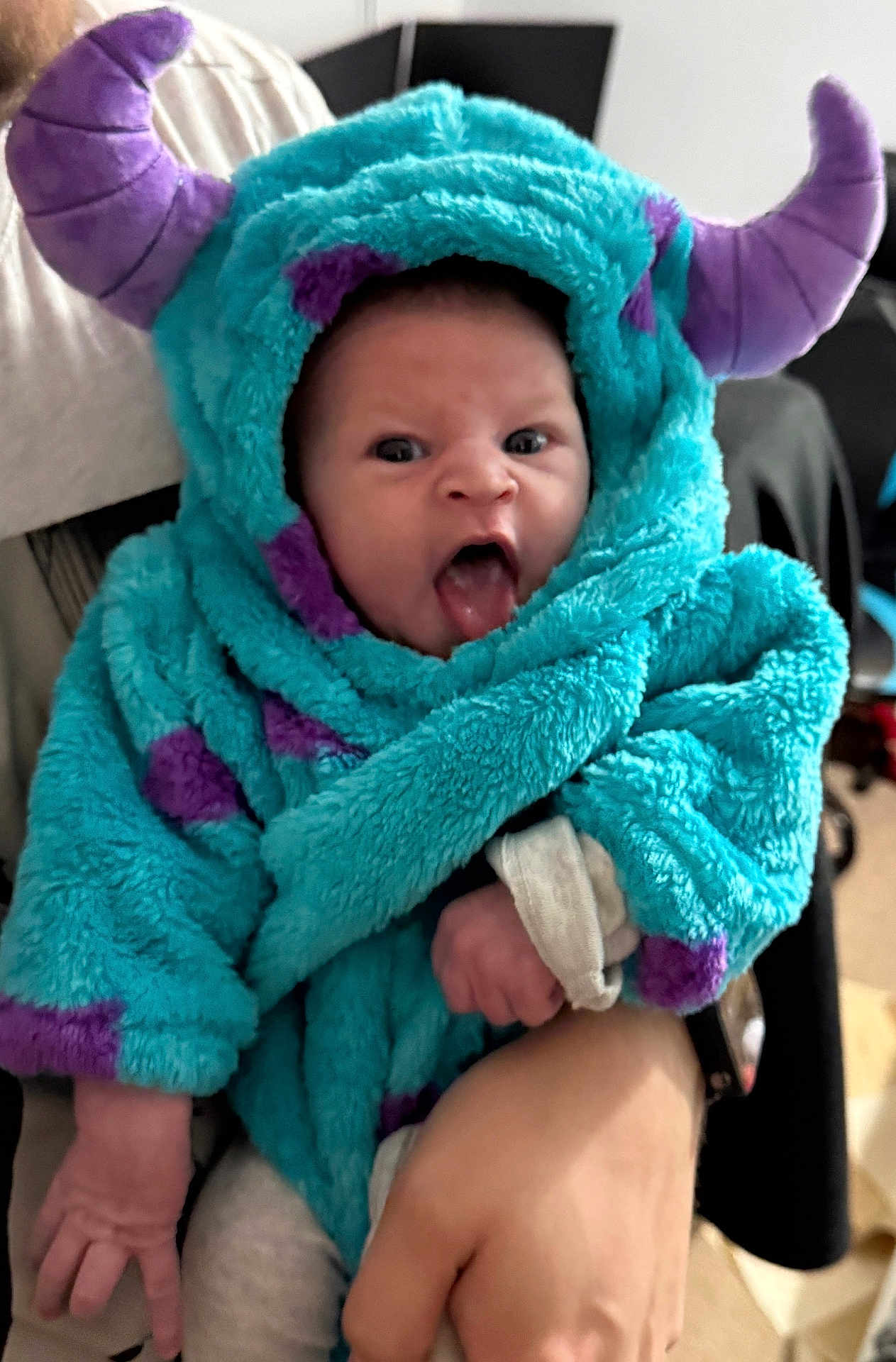 Rowan is registered to the contest to win money with this photo: baby, infant, costume, hood, monster, purple, blue, hand, indoor, cute, tongue_out, expression, clothing, person, child, soft_texture, warm, holding, funny_face, portrait