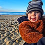 Gauthier participe au concours pour gagner de l'argent avec cette photo : baby, child, smiling, hat, beanie, pom_pom, fleece_jacket, brown_jacket, blue_eyes, sand, beach, ocean, sky, outdoor, cold_weather, happy, portrait, close_up, person, winter_clothing