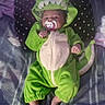 baby, bare_feet, bed, blanket, child, costume, cozy, cute, dinosaur_costume, dragon, face, green_clothing, hood, indoor, infant, lying_down, pacifier, patterned_bedding, portrait, sleeping_area