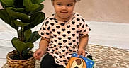 Araya joined the competition — help win amazing prizes! toddler, child, book, toy, plant, potted_plant, rug, floor, chair, indoors, cute, smiling, clothing, hair_tie, patterned_rug, colorful, illustration, sitting, playtime, background
