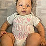 Journey is registered to the contest to win money with this photo: baby, child, curly_hair, onesie, text_on_clothing, lying_down, patterned_blanket, blue_eyes, cute, infant, skin, hand, foot, legs, portrait, indoors, relaxed, expression, pink_text, white_clothing