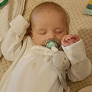 Eddy a rejoint le concours — aidez-le/la à gagner de superbes lots ! baby, sleeping, pacifier, plush_toy, white_onesie, cushion, quilted, infant, hand, face, head, soft_toy, resting, cozy, blanket, cute, indoors, child, peaceful, portrait