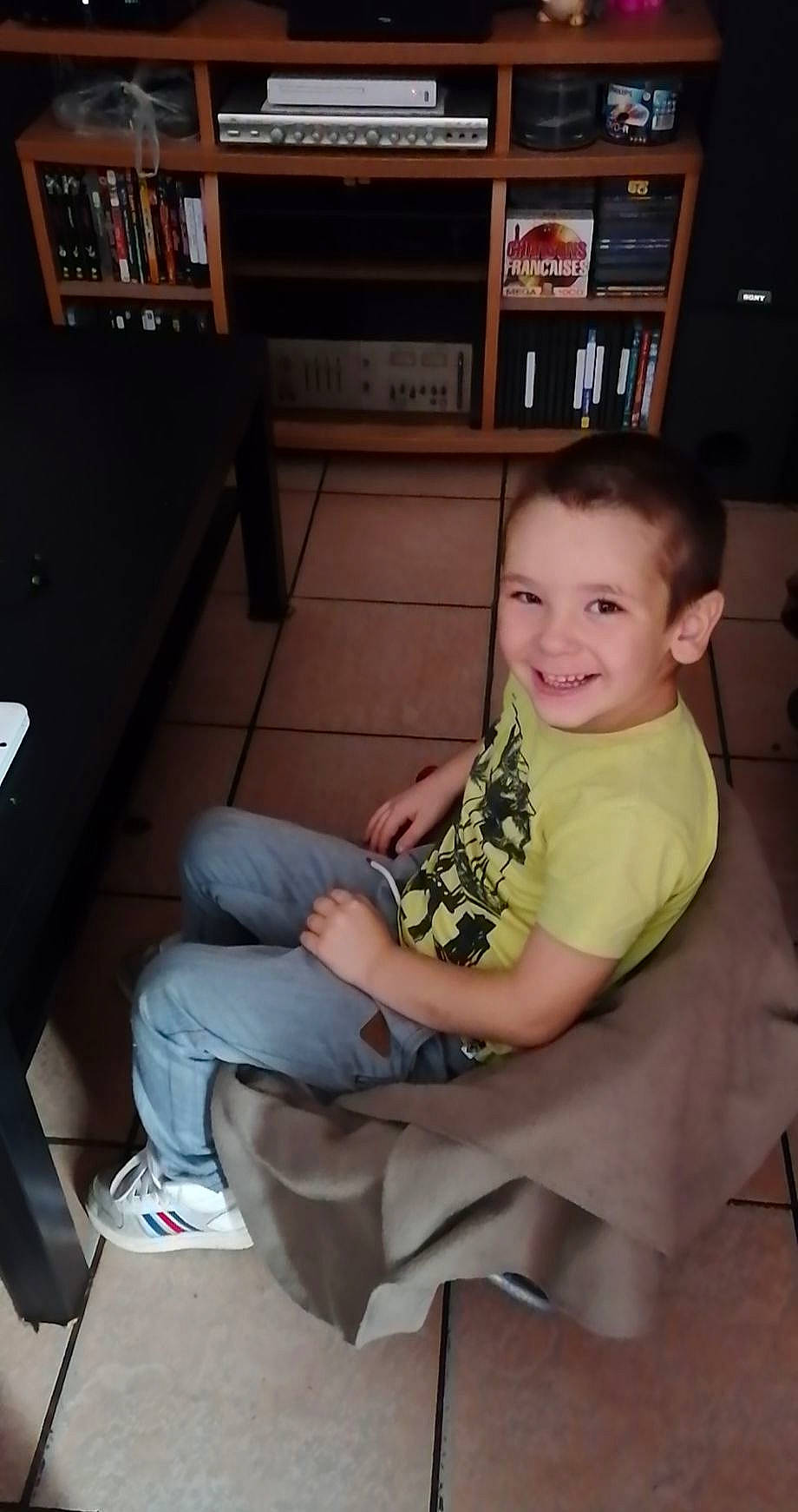 Hugo participe au concours pour gagner de l'argent avec cette photo : ankle, baby_toddler_clothing, bookcase, comfort, denim, foot, jeans, joy, lap, leg, living_room, person, picture_frame, shelf, shelving, shoe, sitting, slipper, sock