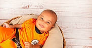 William joined the competition — help win amazing prizes! baby, infant, smile, orange_clothing, basket, cushion, wooden_background, portrait, happy, child, cute, relaxed, indoors, person, head, face, sitting, bright, soft_lighting, cozy