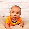 William is registered to the contest to win money with this photo: baby, infant, child, orange_shirt, cushion, soft, portrait, face, cute, expression, indoor, light_skin, short_hair, looking, young, person, head, resting, photography, background