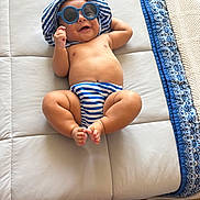William joined the competition — help win amazing prizes! baby, barefoot, blue, child, cushion, cute, happy, hat, headwear, indoor, infant, playful, relaxing, skin, smiling, striped, striped_clothing, sunglasses, toddler, white_background