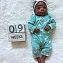 baby, infant, polka_dot, onesie, headband, white_blanket, wooden_blocks, age_marker, lying_down, curious_expression, cute, newborn, soft_texture, hand, foot, buttoned_clothing, portrait, indoor, child, milestone