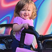 Madi joined the competition — help win amazing prizes! child, toddler, toy_car, purple_shirt, outdoor, smiling, play, vehicle, handle, happy, face, short_hair, daylight, colorful_background, plastic, black_handle, pink, person, cute, portrait