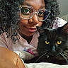 Bynx joined the competition — help win amazing prizes! bed, black_cat, casual_clothing, cat, closeup, companion, curly_hair, cute, face, feline, glasses, human, indoor, person, pet, portrait, relaxed, snuggle, whiskers, yellow_eyes
