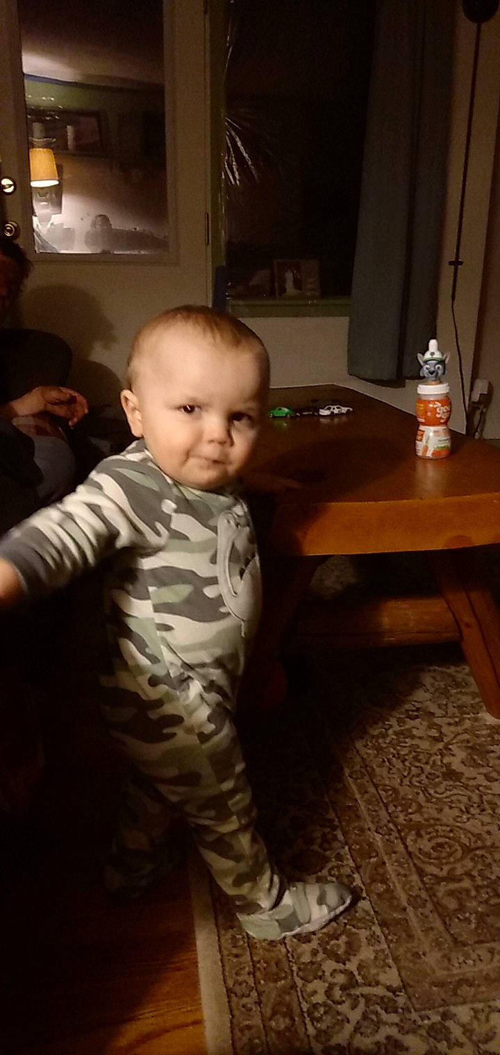 Kaiser is registered to the contest to win money with this photo: baby, baby_toddler_clothing, bottle, child, event, floor, flooring, fun, hardwood, lamp, lighting, living_room, person, picture_frame, room, sitting, standing, table, toddler, water_bottle