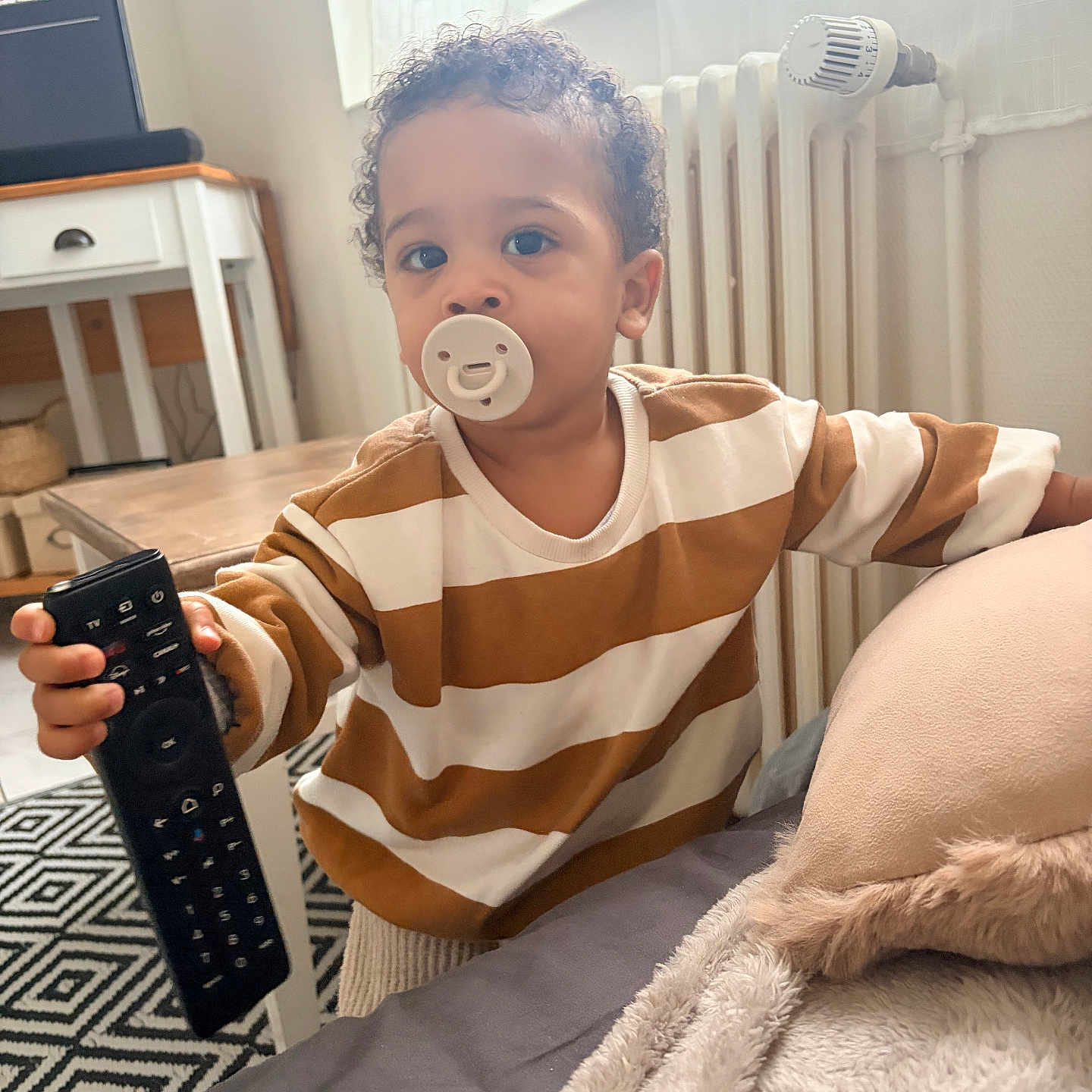 Gabriel a rejoint le concours — aidez-le/la à gagner de superbes lots ! bed, blanket, carpet, chair, child, cozy, curly_hair, curtains, furniture, home, indoor, pacifier, person, pillow, radiator, remote_control, striped_shirt, table, toddler, window