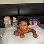 baby, child, curly_hair, pillow, plush_toy, stuffed_animal, mickey_mouse, lion_toy, bedroom, indoor, infant, cute, wide_eyes, portrait, furniture, soft_toys, couch, skin, expression, resting