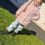 Peyton participe au concours pour gagner de l'argent avec cette photo : child, girl, braids, pink_coat, fur_hood, jeans, black_shoes, grass, shadow, sidewalk, outdoor, sunny, daylight, wall, curious_expression, person, casual_clothing, standing, nature, winter_clothing