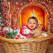Alan a rejoint le concours — aidez-le/la à gagner de superbes lots ! baby, basket, teddy_bear, christmas, fireplace, holiday_decorations, red_and_white_clothing, smiling, festive, pine_branches, gift_boxes, indoor, portrait, wooden_floor, cozy, toy, child, warm_lighting, decorative_ribbons, snowflake_ornaments