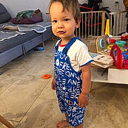 Léandre a rejoint le concours — aidez-le/la à gagner de superbes lots ! baby_gate, barefoot, blue_overall, casual, child, couch, face, floor, hair, home, indoor, living_room, person, pillow, playful, standing, table, toddler, toys, white_shirt