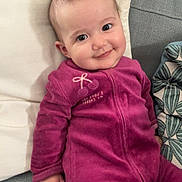 Thaïs participe au concours pour gagner de l'argent avec cette photo : baby, child, smiling, onesie, purple_clothing, couch, pillow, indoor, cute, face, person, infant, seated, happy, soft_fabric, hand, head, eyes, home, cozy