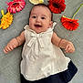 baby, black, child, colorful, cream_flower, cute, dress, face, flower, gerbera, happy, indoor, laying_down, orange_flower, pink_flower, portrait, red_flower, smiling, white, yellow_flower