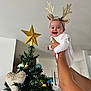 baby, celebration, child, christmas, christmas_tree, cute, decoration, festive, golden_star, hands, happy, holding, holiday, indoor, ornaments, person, reindeer_antlers, smile, tree, white_clothing
