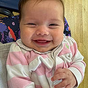 Olivia joined the competition — help win amazing prizes! baby, smiling, face, child, pink_clothing, striped_clothing, hand, cushion, chair, wood_floor, happy, cute, infant, portrait, indoors, person, sitting, closeup, joy, expression